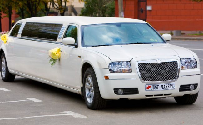 White wedding limousine on the road. Ornated with flowers.